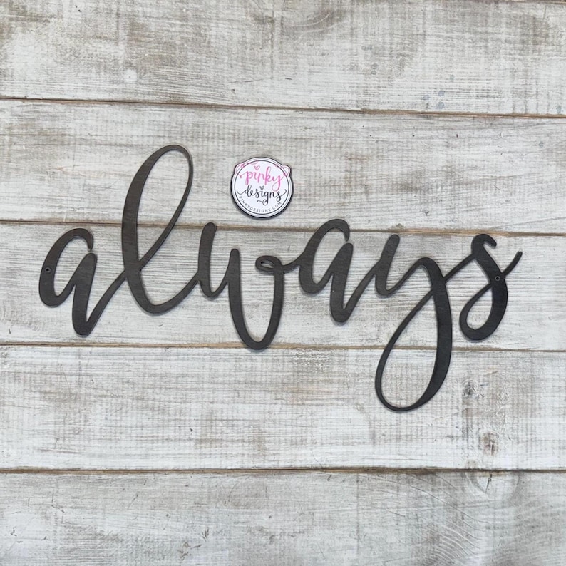 May include: Black metal wall decor with the word "always" written in a cursive font. The decor is mounted on a white wood background.