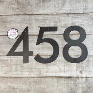 May include: Black metal house numbers 4, 5, and 8. The numbers are cut out and have a rustic look.