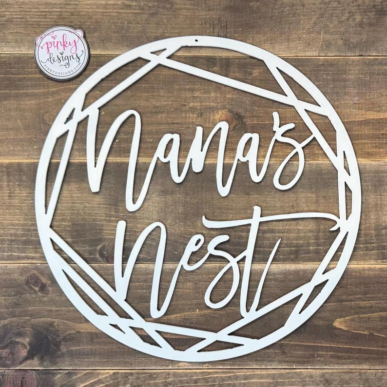 May include: White wooden sign with a geometric design and the words "Mama's Nest" in a cursive font.