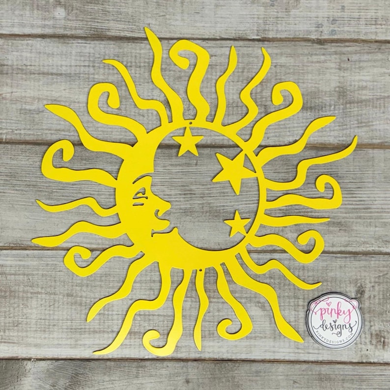 May include: Yellow metal sun and moon wall art with a crescent moon and three stars. The sun has a face and rays. The art is on a wood background.