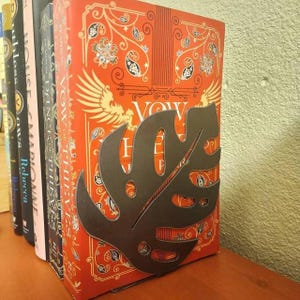 A metal monstera leaf bookend that is supporting a stack of books behind it