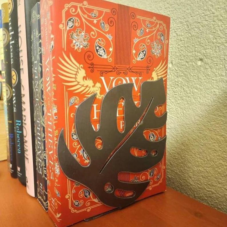 A metal monstera leaf bookend that is supporting a stack of books behind it