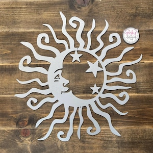 May include: A silver metal sun and moon wall decor with a stylized face on the moon and stars. The sun has a swirling design.