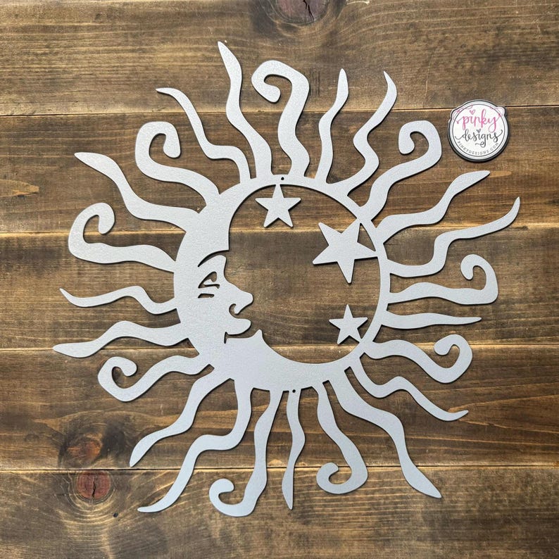 May include: A silver metal sun and moon wall decor with a stylized face on the moon and stars. The sun has a swirling design.