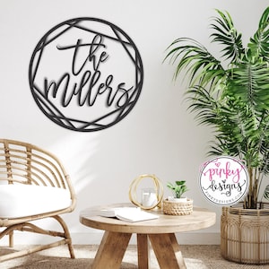 Large metal wall art piece mounted on a light interior of a home. Below is a boho looking living room. There is a wick chair on the left side of the room next to a light wooden table, a wick planter sits to the right with a large plant inside of it.