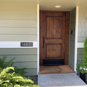 There is a modern rectangular house number sign. The address sign is left raw metal and reads 14805. The sign is mounted on a light green exterior of a home on the only piece that's painted white.