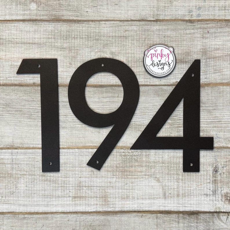 May include: Black metal house numbers 194 on a light wood background. The numbers are attached with screws.