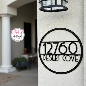 May include: Black metal house number sign with a circular frame. The sign displays the number 12760 and the text "DESERT COVE".