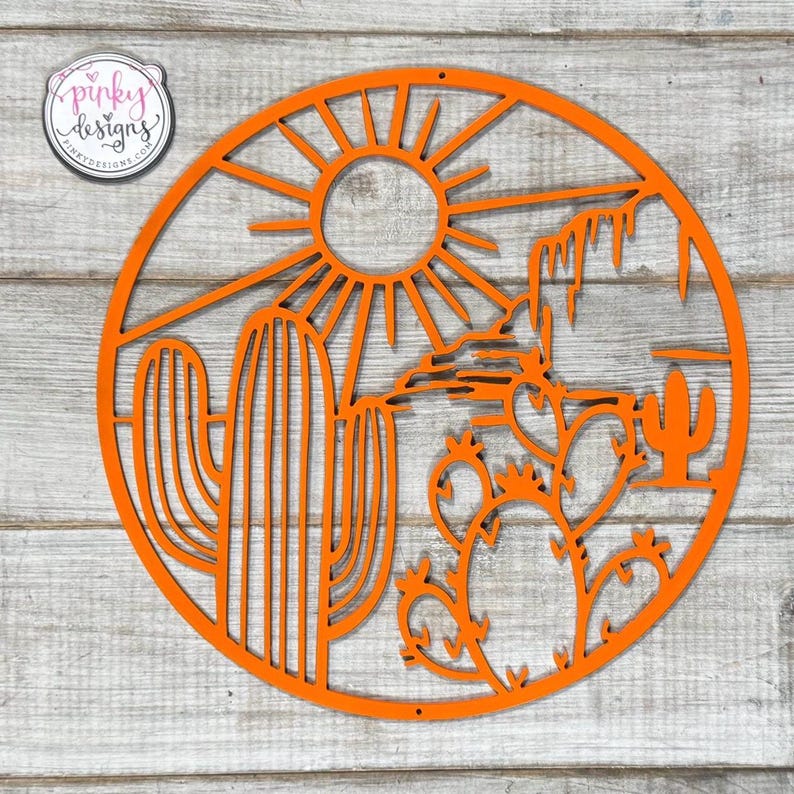 May include: Orange metal wall art featuring a desert scene with a sun, mountains, and cacti. The art is circular and has a cutout design.