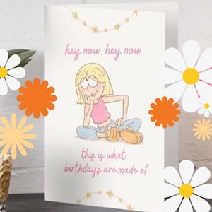 May include: A white greeting card featuring a cartoon illustration of a blonde character sitting down, wearing a pink top and blue pants. The text reads, "hey now, hey now" at the top and "this is what birthdays are made of" at the bottom in pink.