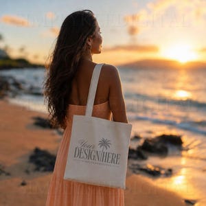 Puede incluir: Un bolso de tela beige con un gráfico gris oscuro de una palmera y el texto "YOUR DESIGN HERE" impreso en la parte delantera. El bolso tiene dos asas y lo lleva una persona con un vestido de color melocotón durante el atardecer.