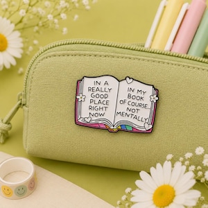 Open book hard enamel pin attached to a sage green pencil case surrounded by pastel pens and daisy flowers. Funny book lover enamel badge reading "In a really good place right now... in my book of course, not mentally." Perfect teacher gift, librarian gift, reader accessory, backpack pin and stationery lover gift.