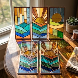 May include: A collection of stained glass panels depicting a sunrise over a landscape. The panels feature a variety of colors, including blues, greens, oranges, and yellows. Each panel has a copper frame and a hanging loop.