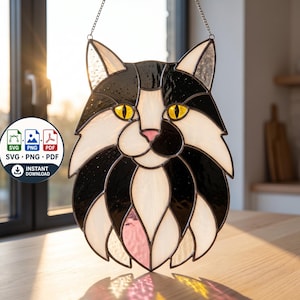 May include: A stained glass suncatcher shaped like a cat head with black and white glass segments, bright yellow eyes, and a pink nose. The piece is outlined in dark metal solder and hangs from a thin silver chain, featuring a digital file download icon.
