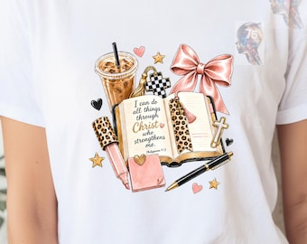 May include: A white t-shirt featuring a graphic print of an open book with the text I can do all things through Christ who strengthens me. Philippians 4:13, a coffee cup, a pink bow, a leopard print pen, a sticky note, a black pen, and stars.
