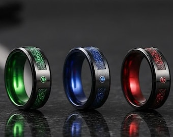 May include: Three rings with black outer bands and colored inner bands in green, blue, and red. Each ring features a textured inlay pattern and a single small circular stone matching the inner color, set into the black metal surface.
