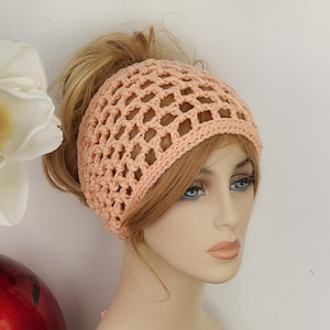 May include: A peach-colored crochet hair net with an open, grid-like pattern. The accessory is worn on a mannequin head with light brown hair styled in a high ponytail, featuring a solid, thicker band around the forehead and a mesh design.