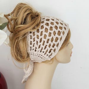 May include: A crocheted headband in a light beige color with a delicate openwork pattern. The headband is tied at the back of the head with two long ties.