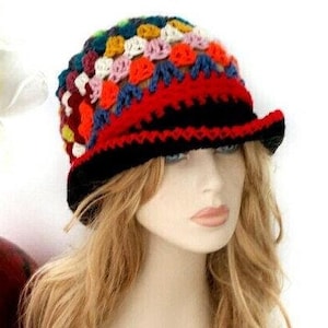 May include: A colorful crochet hat with a black brim and a red band. The hat features a patchwork design with various colors, including red, blue, yellow, and white. The hat is a unique accessory.