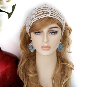 May include: A cream-colored crocheted headband with a striped design. The model is wearing turquoise teardrop earrings. A red vase with white flowers is in the background.