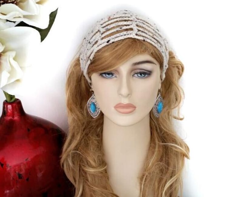 May include: A cream-colored crocheted headband with a striped design. The model is wearing turquoise teardrop earrings. A red vase with white flowers is in the background.
