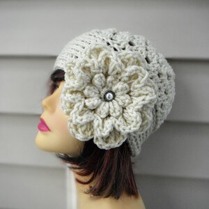 May include: A white crocheted beanie with a large white crocheted flower on the side. The flower has a pearl-like button in the center.