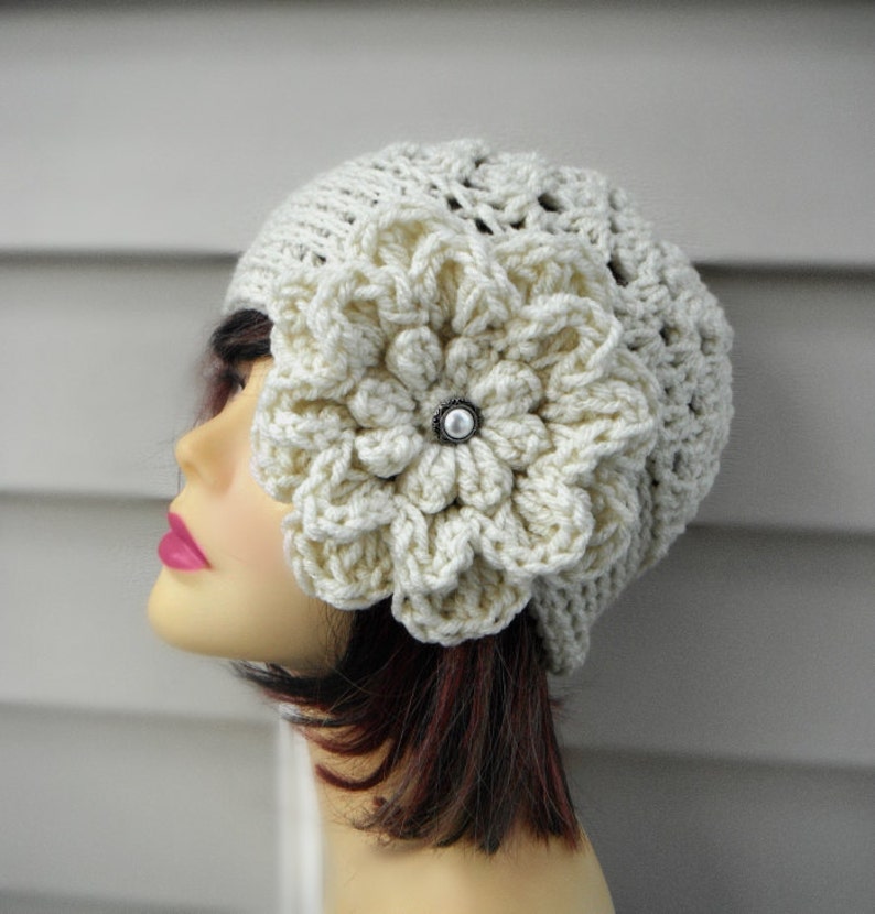 May include: A white crocheted beanie with a large white crocheted flower on the side. The flower has a pearl-like button in the center.