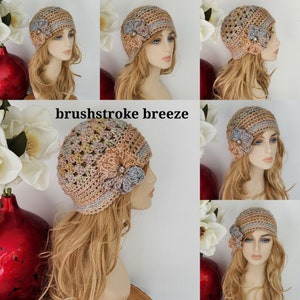 May include: A crocheted hat with a flower embellishment in shades of pink, beige, and blue. The hat has a slouchy, beanie style and is made with a textured stitch.