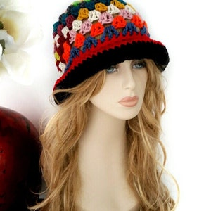 May include: A colorful, handmade crochet hat with a black brim. The hat features a patchwork design with various colors, including red, blue, yellow, and pink. This unique hat is a stylish accessory.