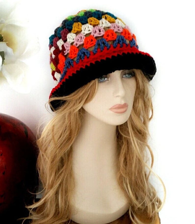 May include: A colorful, handmade crochet hat with a black brim. The hat features a patchwork design with various colors, including red, blue, yellow, and pink. This unique hat is a stylish accessory.