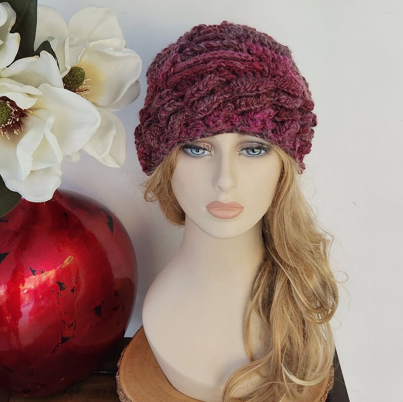 May include: A close-up of a pink and purple crocheted beanie hat on a mannequin head with long, wavy, light brown hair.
