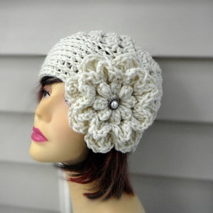 May include: A white crocheted beanie with a large white crocheted flower on the side. The flower has a pearl-like button in the center.