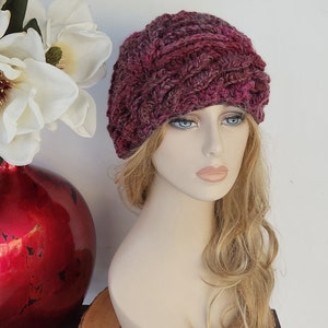 May include: A pink and purple crocheted headband with a braided design. The headband is worn on a mannequin with long, wavy, blonde hair.