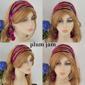 May include: A purple and red crocheted headband with a knotted design. The headband is worn by a mannequin with long blonde hair.