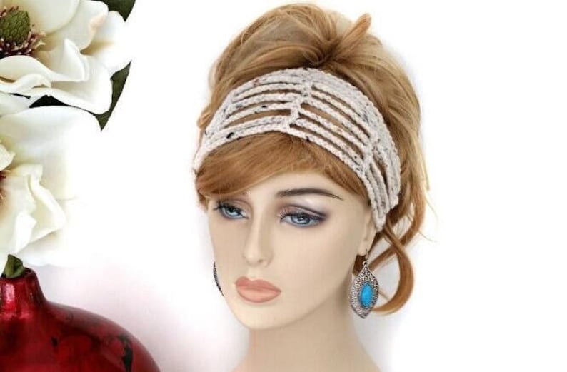 May include: A cream-colored, open-weave headband with a speckled pattern. The headband is worn on a mannequin with blonde hair and blue eyes. The mannequin also wears turquoise earrings.