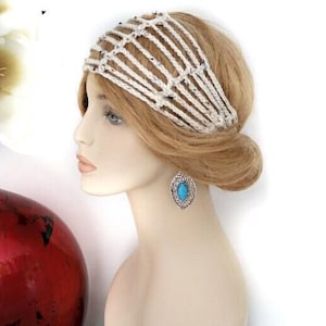 May include: A mannequin head with blonde hair and a cream-colored crocheted headband. The mannequin is wearing a silver-toned earring with a turquoise stone. A red vase with white flowers is in the background.