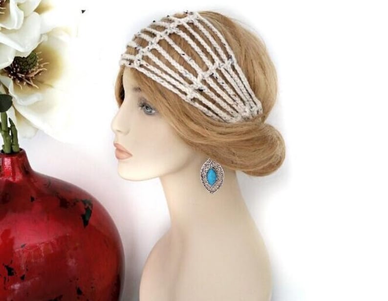 May include: A mannequin head with blonde hair and a cream-colored crocheted headband. The mannequin is wearing a silver-toned earring with a turquoise stone. A red vase with white flowers is in the background.