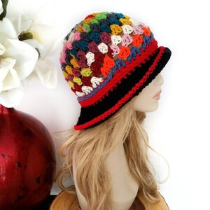 May include: A colorful, handmade crochet hat with a brim. The hat features a patchwork design with squares of various colors, including red, black, blue, yellow, and white. The brim is black with a red trim. This hat is a unique accessory.