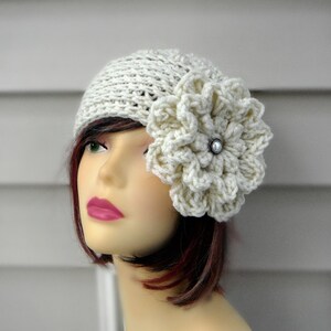 May include: A white crocheted hat with a large white crocheted flower on the side. The flower has a pearl-like button in the center.
