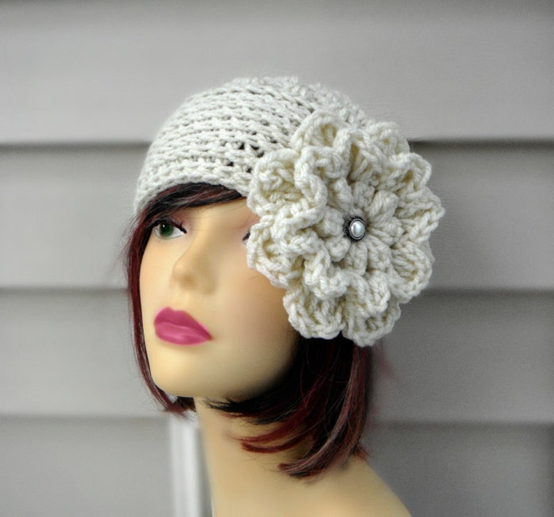 May include: A white crocheted hat with a large white crocheted flower on the side. The flower has a pearl-like button in the center.