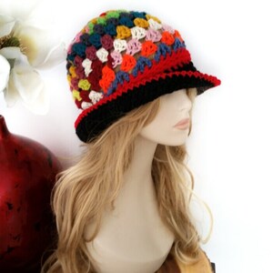 May include: A colorful crochet hat with a brim. The hat features a patchwork design in various colors, including red, black, blue, orange, and white. The brim is black with a red border. This handmade hat is a unique accessory.