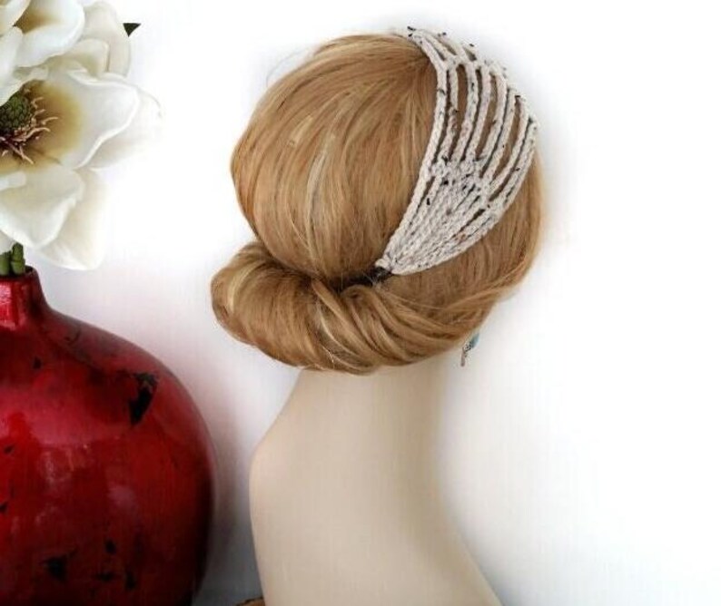 May include: A cream-colored, beaded headband with a unique, open design is worn in the hair. The hair is styled in a low bun. A red vase with white flowers is in the background.