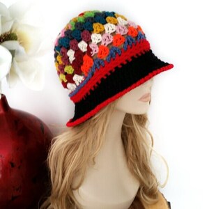 May include: A colorful crochet bucket hat with a black brim and red trim. The hat features a patchwork design with squares of various colors, including red, blue, yellow, and green. The hat is a stylish accessory.