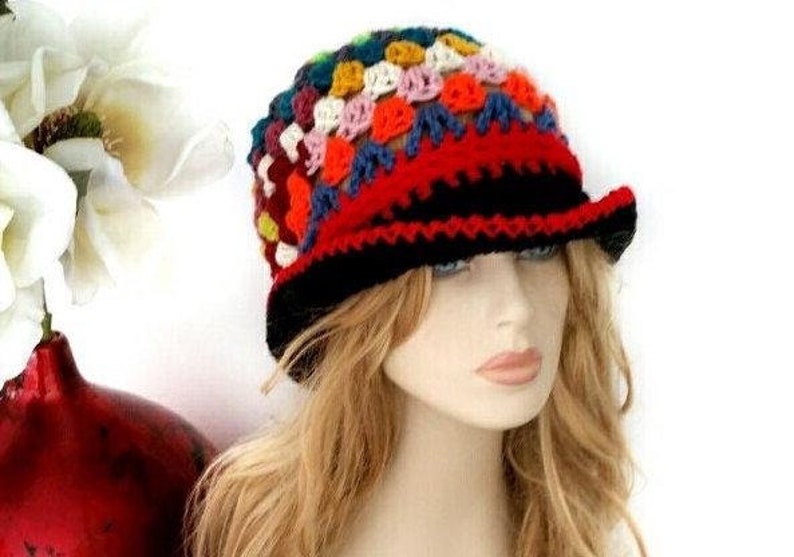 May include: A colorful crochet hat with a black brim and a red band. The hat features a patchwork design with various colors, including red, blue, yellow, and white. The hat is a unique accessory.