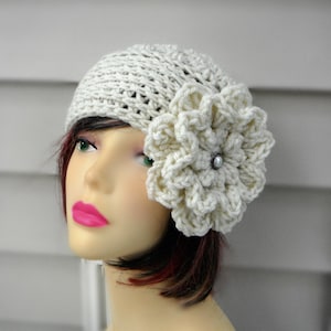 May include: A white crocheted beanie with a large white crocheted flower on the side. The flower has a pearl-like button in the center.