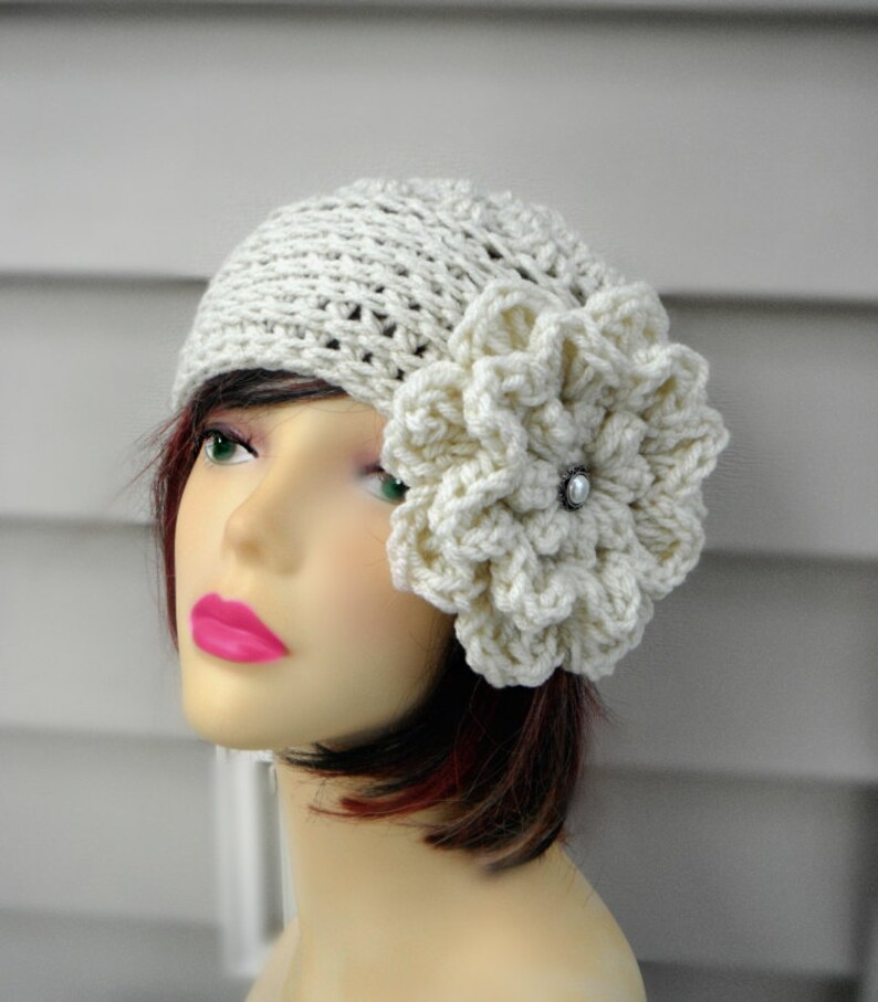 May include: A white crocheted beanie with a large white crocheted flower on the side. The flower has a pearl-like button in the center.
