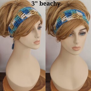 May include: A 3-inch wide crochet headband featuring a variegated pattern of blue, teal, tan, and white yarn. The accessory is displayed on a mannequin head, showcasing the open-weave texture and the tie-back design with dangling ends.