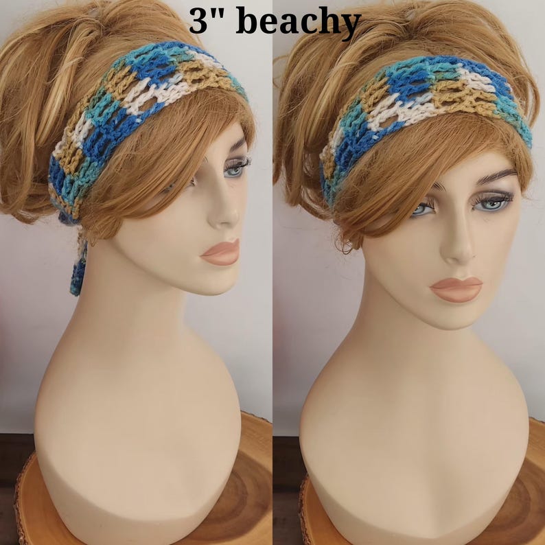May include: A 3-inch wide crochet headband featuring a variegated pattern of blue, teal, tan, and white yarn. The accessory is displayed on a mannequin head, showcasing the open-weave texture and the tie-back design with dangling ends.