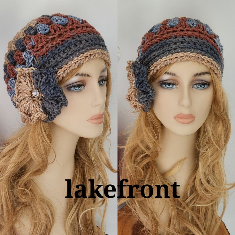 May include: A crocheted beanie with a flower detail in shades of brown, gray, and blue. The beanie has a slouchy fit and is made with a textured stitch.