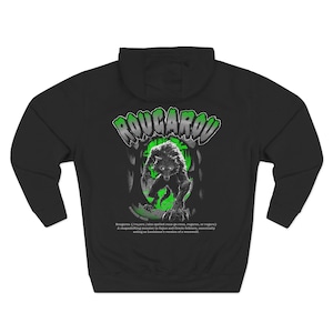 May include: A black hooded sweatshirt featuring a graphic on the back with the text ROUGAROU in a stylised font. The design depicts a wolf-like creature in a green forest setting, with descriptive text below explaining the folklore of the monster.